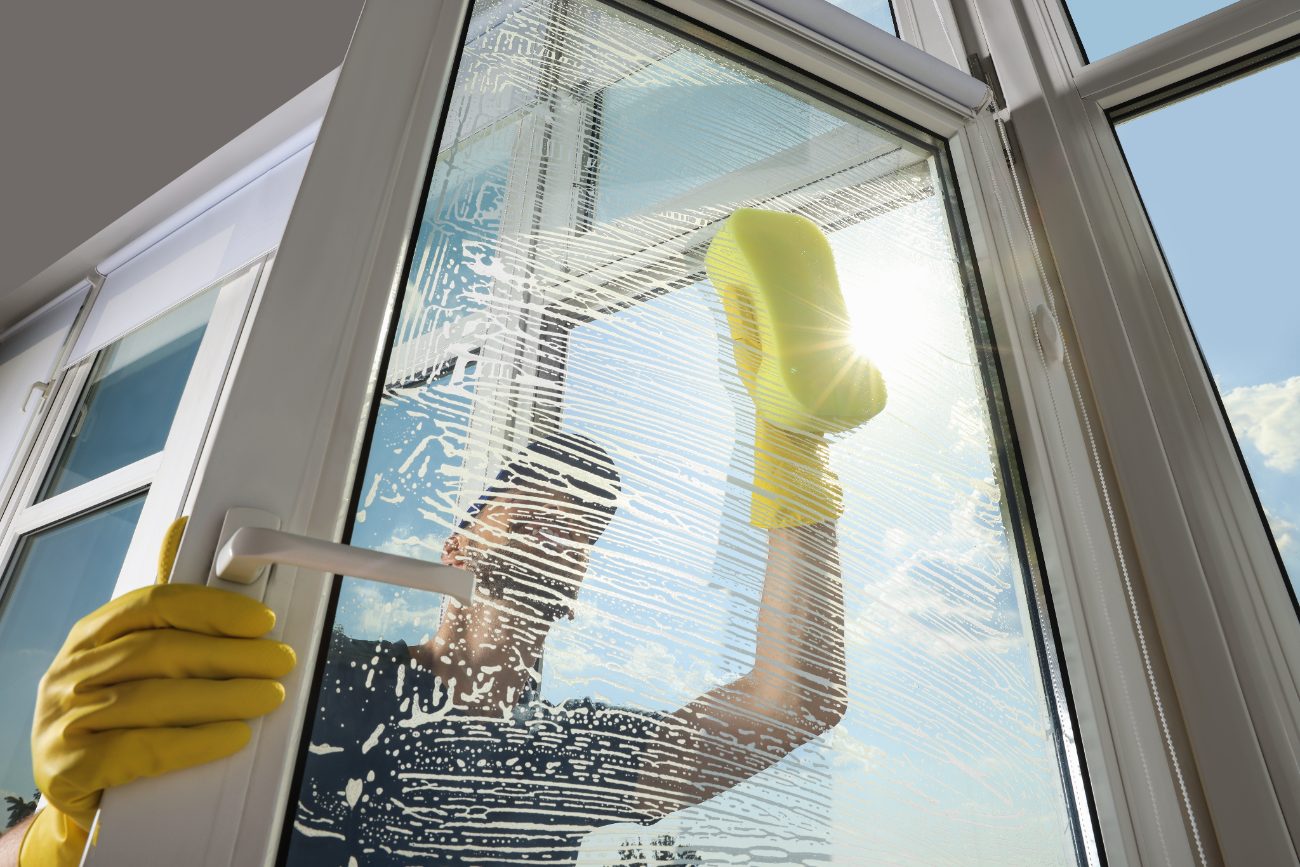 Person in yellow gloves cleaning large window with squeegee on sunny day