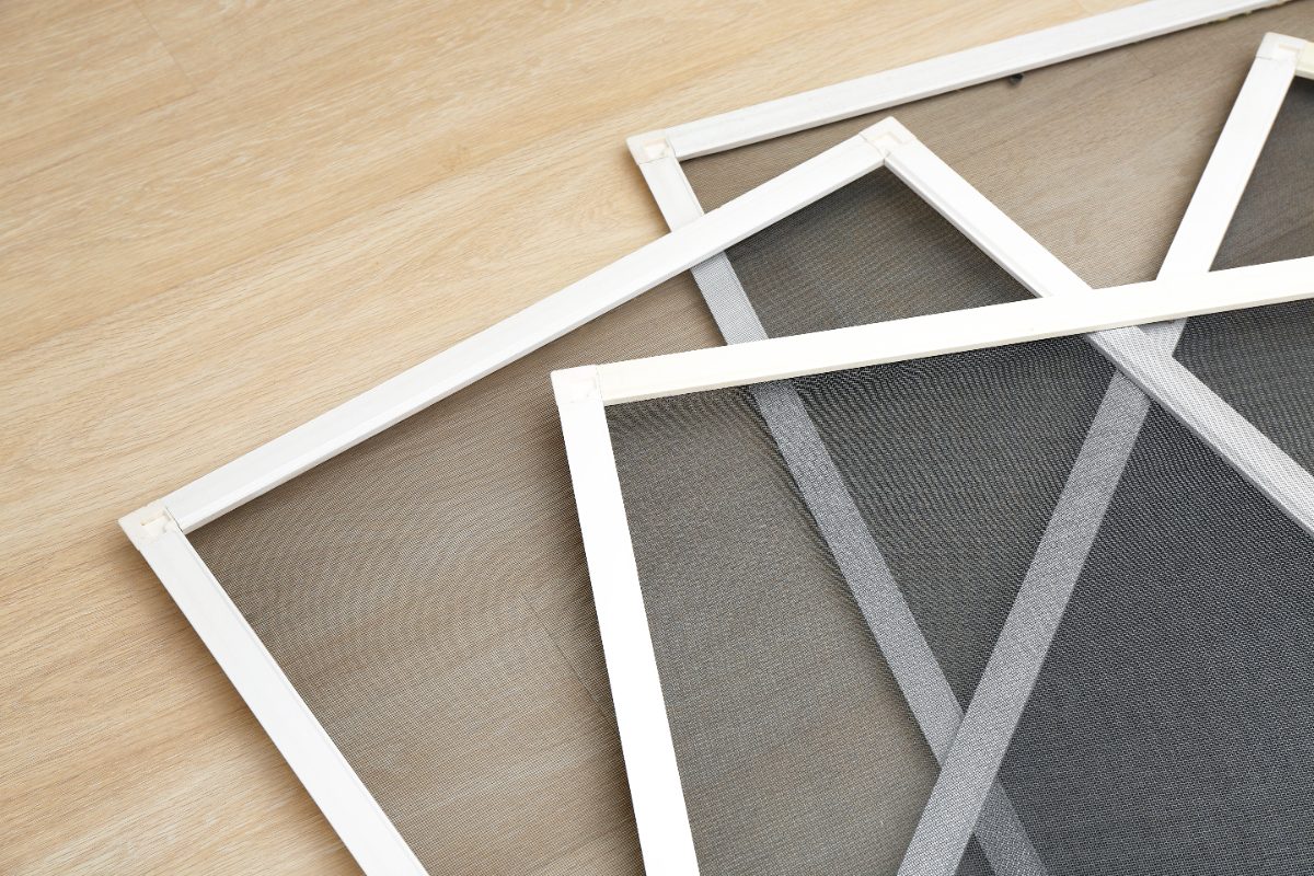 White window screen frames with gray mesh material on wooden surface